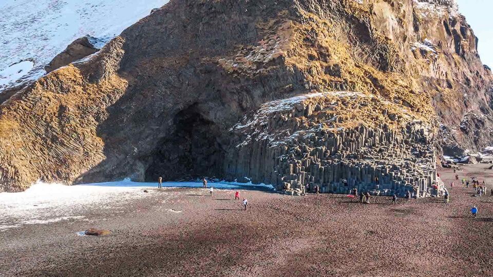 big cave in a cliff on a black beach