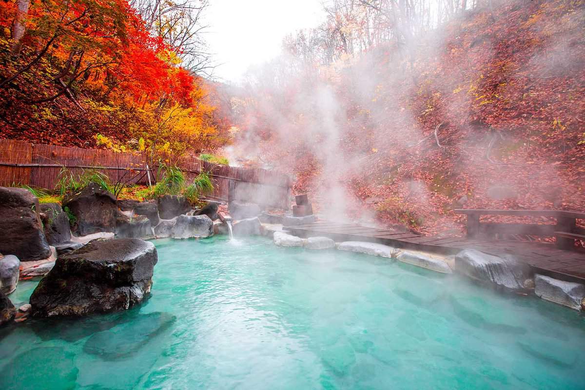 steaming outdoor thermal pool surrounded by red acer trees