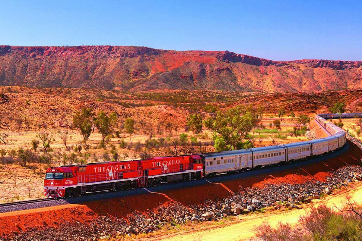 The red Ghan train travelling through a stark desert landscape