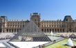 Landscape view of Louvre Museum outside building with the famous glass pyramid structure against a sunny blue day